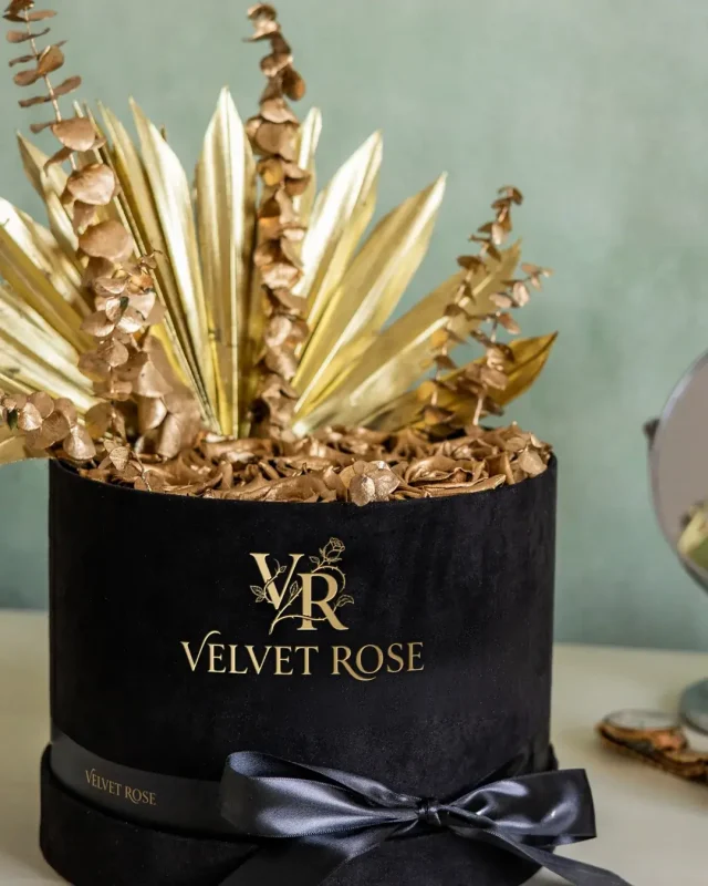 Gold preserved roses in a black velvet hat box with gold palm leaves